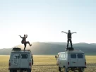 Duas pessoas em pé sobre vans em um campo aberto ao pôr do sol, celebrando a liberdade de viajar.