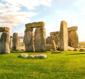 Formação de pedras monumentais de Stonehenge ao entardecer, com céu parcialmente nublado e gramado verde ao redor.