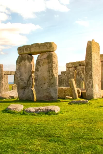 Formação de pedras monumentais de Stonehenge ao entardecer, com céu parcialmente nublado e gramado verde ao redor.