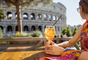 Mulher aprecia uma bebida ao ar livre com vista para o Coliseu em Roma durante um dia ensolarado de verão.