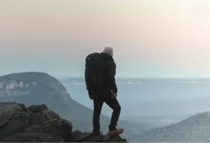 Pessoa em trilha observa o horizonte montanhoso ao entardecer.**