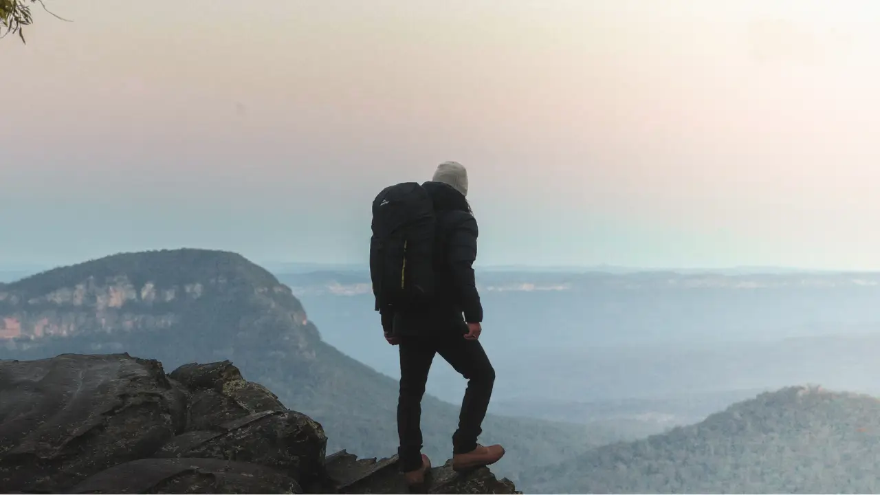 Pessoa em trilha observa o horizonte montanhoso ao entardecer.**