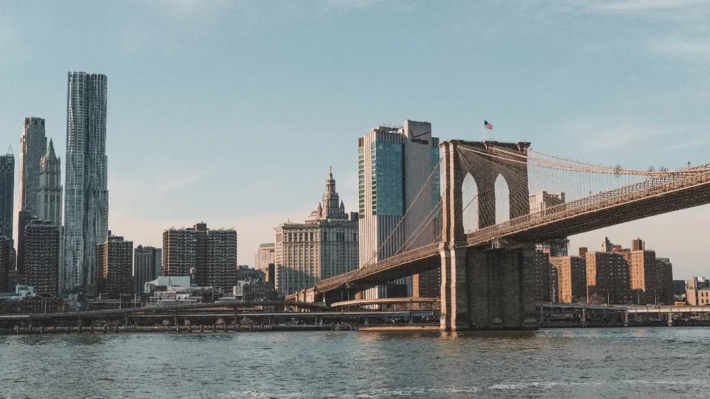 Ponte de Brooklyn com skyline de Manhattan ao fundo, vista do harborside, em dia claro.