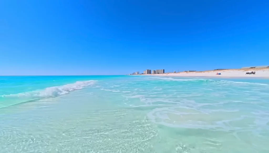 "Águas cristalinas verde-esmeralda de Destin, Florida, com areia branca como açúcar, ondas suaves e arranha-céus ao fundo sob céu azul perfeito"