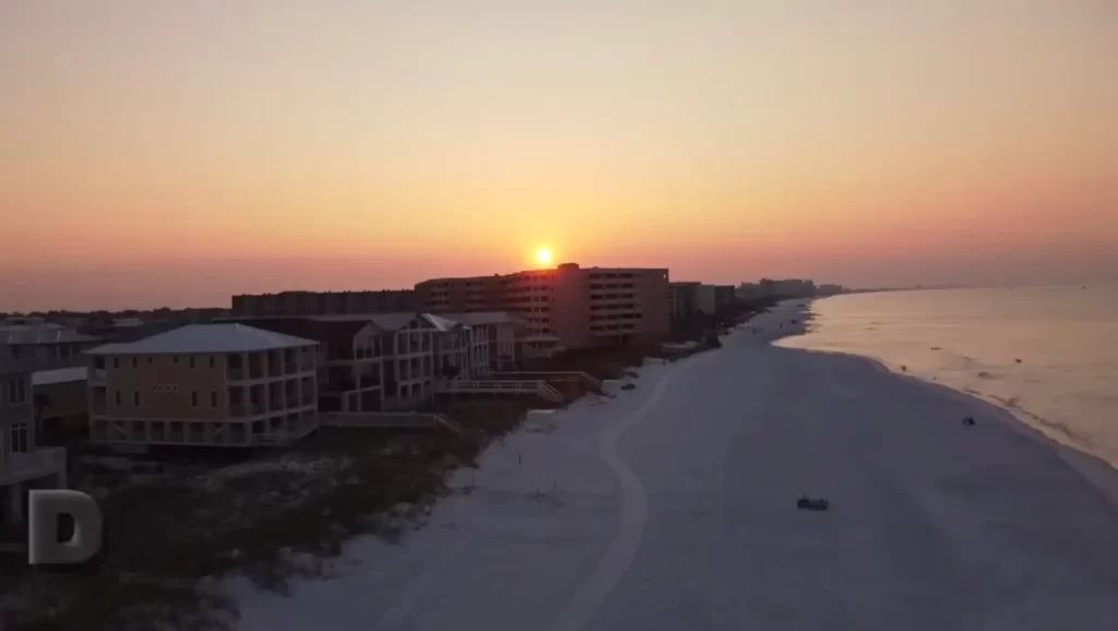"Pôr do sol dourado sobre as praias de areia branca de Destin, Florida, com resorts à beira-mar e céu em tons de laranja e rosa refletindo no Golfo do México"